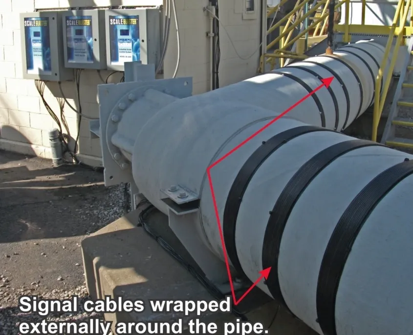 ScaleBlaster signal cables wrapped around large pipe for external scale prevention treatment.
