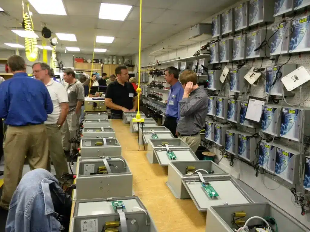 Visitors tour ScaleBlaster production area with units on workbenches and assembled on display wall.
